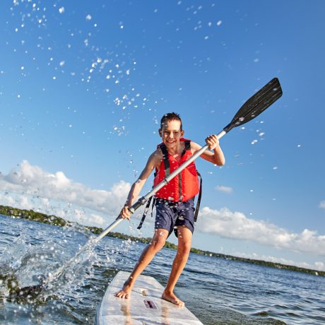 happy boy paddling on stand up paddleboard. cheerful child having fun on water. Summer vacation leisure activity, SUP boarding
