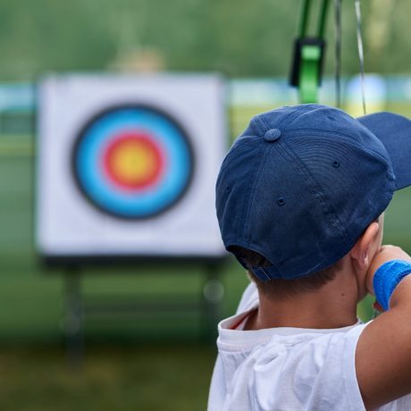 Young boy aims at a target with his bows and arrows